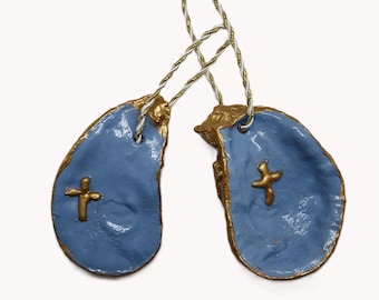 May include: Two blue, teardrop-shaped ornaments with gold trim and a gold cross. The ornaments are connected by a twisted gold and white string. The ornaments are likely handmade and have a rustic appearance.