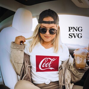 Può includere: Una donna indossa una maglietta bianca con una grafica rossa "Cool", un cappello da baseball nero e leggings marroni. Sta tenendo una bevanda al caffè in un bicchiere trasparente con un coperchio marrone.