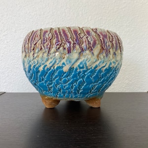 May include: A blue and purple ceramic planter with a textured surface and three legs.