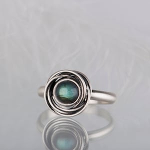 May include: A silver ring with a swirling design and a green and blue gemstone in the center.