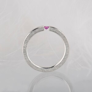 May include: A silver ring with a textured finish and a small pink gemstone set in the center.