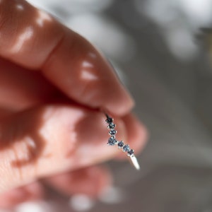 May include: A silver ring with a curved design featuring a row of small blue gemstones.