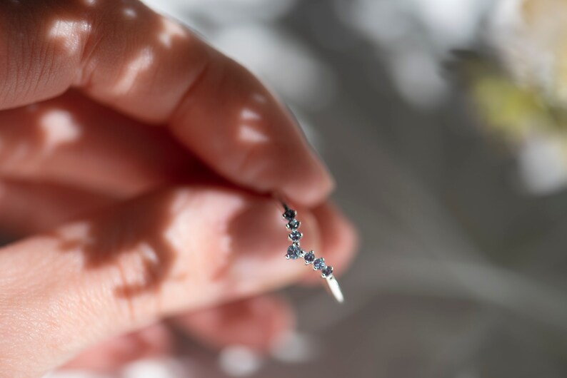 May include: A silver ring with a curved design featuring a row of small blue gemstones.