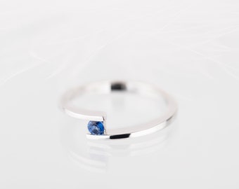 Puede incluir: Un anillo de banda de plata simple con una sola piedra preciosa de zafiro azul engastada en el centro.