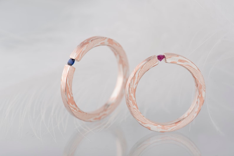 Two mokume gane sterling silver and copper tension engagement rings - one with natural blue sapphire and one with natural deep pink ruby