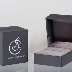 May include: A gray jewelry box with a white logo that says "Slow Silver Jewelry". The box is open and the inside is lined with gray velvet.