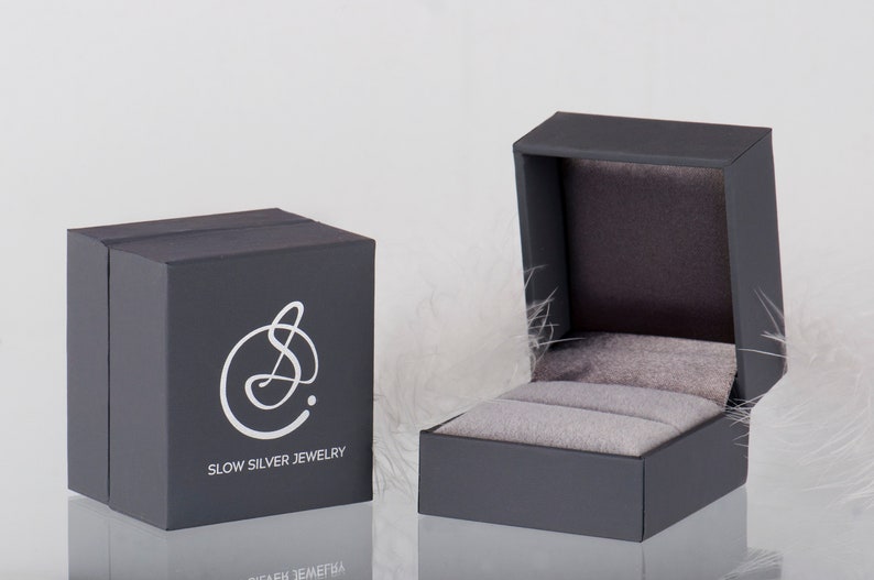 May include: A gray jewelry box with a white logo that says "Slow Silver Jewelry". The box is open and the inside is lined with gray velvet.