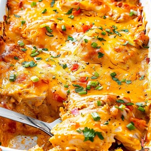Może przedstawiać: Zapieczona potrawa w białym prostokątnym naczyniu zawierająca rozdrobnionego kurczaka, roztopiony pomarańczowy ser cheddar, pokrojoną w kostkę czerwoną paprykę oraz posypkę z posiekanego szczypiorku i świeżej kolendry, z metalową łyżką do serwowania.