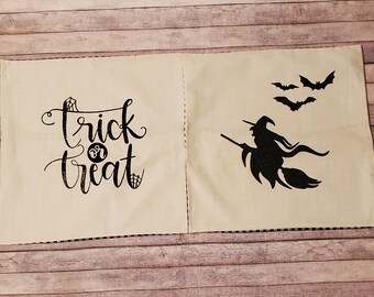 May include: Two cream-colored Halloween-themed pillow covers. One features the words "trick or treat" in black script with spiderweb accents. The other has a black glitter witch on a broom and three bats.