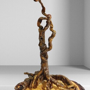 Peut inclure: Une sculpture verticale fabriqu&eacute;e &agrave; partir d'une racine d'arbre brune, polie et torsad&eacute;e, qui s'&eacute;tire vers le haut en une branche fine et courb&eacute;e. La structure racinaire est fix&eacute;e sur une base en bois clair avec des cernes visibles.