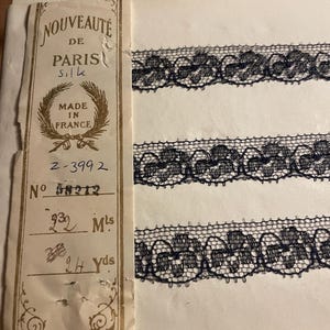 Può includere: Un primo piano di un'etichetta per un pizzo nero. L'etichetta recita "NOUVEAUTÉ DE PARIS Silk MADE IN FRANCE" e include i numeri "2-3992" e "58212". L'etichetta include anche le misure "22 Mls" e "24 Yds".