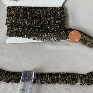 May include: A spool of black and gold beaded fringe trim. The fringe is approximately 2.5 cm wide and is shown next to a UK penny for scale.