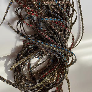 May include: A tangled pile of decorative trim with a metallic gold base. The trim is embellished with small, colorful beads in red, blue, and pink. The trim is likely used for sewing, crafting, or embellishing clothing.