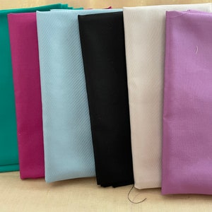 May include: A stack of six fabric swatches in different colors: teal, magenta, light blue, black, off-white, and lavender.