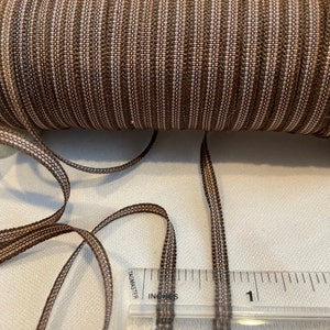May include: A close-up of brown and beige striped elastic trim with a ruler showing it is 1 inch wide.