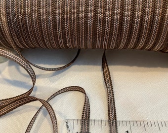 May include: A close-up of brown and beige striped elastic trim with a ruler showing it is 1 inch wide.