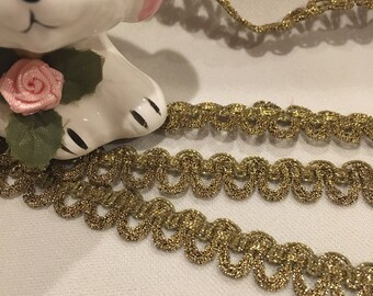 May include: Gold metallic trim with a scalloped edge. The trim is made of a woven fabric with a shiny finish.