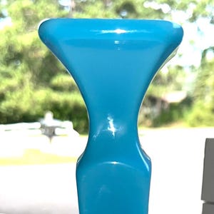 May include: A solid, light blue object with a wide, flat base and a tall, slender stem that flares out at the top. The object is made of a glossy material and has a smooth, reflective surface. The overall shape is reminiscent of a stylized candle holder.