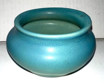 Könnte beinhalten: Eine kleine, runde, türkisfarbene Keramikschale mit einer weiten Öffnung. Die Schale hat eine glatte, matte Oberfläche und eine leicht strukturierte Oberfläche. Der Innenraum ist ein hellerer Türkiston. Diese dekorative Schale eignet sich zum Halten kleiner Gegenstände.