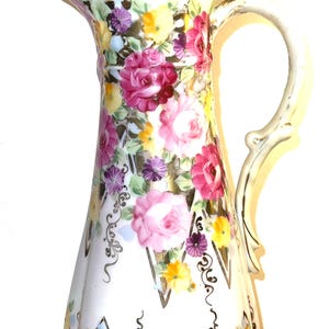 Peut inclure: Pichet en céramique blanche avec un motif floral de roses roses, jaunes et violettes. Le pichet a une poignée incurvée et un couvercle avec une poignée en forme de nœud. Le bord est orné d'accents turquoise et dorés. Un objet décoratif pour la maison.