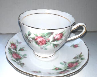 Può includere: Servizio da tè bianco con motivo floreale a rose. La tazza e il piattino hanno un bordo dorato. La tazza presenta un manico ed è decorata con rose rosa e foglie verdi. Il piattino ha un bordo smerlato e un design a rose abbinato.