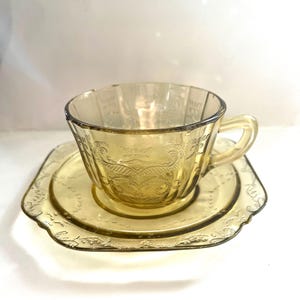 May include: A vintage amber glass teacup and saucer set with a delicate floral pattern. The set is in excellent condition and would be a beautiful addition to any tea lover's collection.
