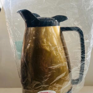 May include: Gold-colored thermal carafe with a black lid and handle. The carafe has a "CAUTION" label that reads "Maximum Dishwashing Water Temperature Shall Not Exceed 160°F (71°C)".