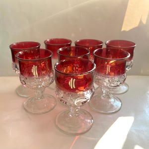May include: Set of eight red glass stemmed drinking glasses with a textured design. The glasses have a clear base and a red, iridescent top.
