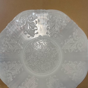 Puede incluir: Un tazón de servir de vidrio blanco esmerilado con un diseño floral en relieve. El tazón tiene un borde festoneado y un fondo ligeramente redondeado.