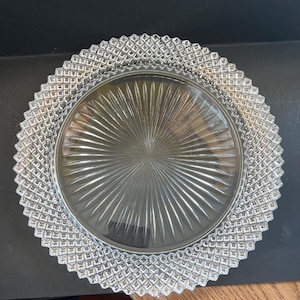 Puede incluir: Plato de vidrio transparente con un borde con diseño de diamantes y un diseño radial en el centro. El plato es circular y parece estar hecho de vidrio. El plato es probablemente para servir comida.