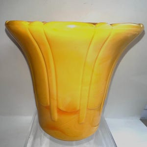 May include: A bright yellow and orange glass vase with a flared, scalloped rim and vertical raised ridges extending from the top down to the mid-section. The glass features a marbled, swirled color pattern throughout the body of the vessel.