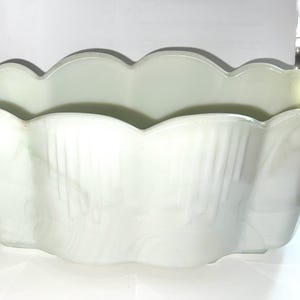 May include: A pale green, scalloped-edge planter with a rectangular shape. The planter has vertical ribbed detailing on the sides and a smooth, glossy finish. The interior is empty, ready for plants or other decorative items.