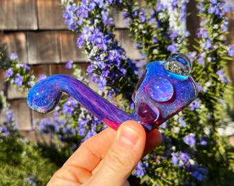 May include: A glass pipe with a iridescent blue and purple finish. The pipe has a round bowl and a curved stem.