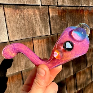 May include: A pink and purple glass pipe with a swirl design and three glass marbles. The pipe has a long, curved stem and a round bowl.