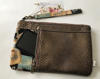 May include: A brown faux leather clutch with a zipped pocket and a snakeskin pattern. The clutch has a matching fabric wrist strap with a floral and vintage postcard print. The strap has a metal clasp and the text "Ettie & Jones Handmade" is printed on a tag attached to the strap.