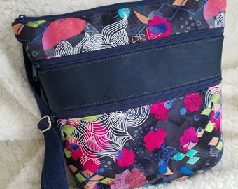 May include: A black crossbody bag with a colourful abstract print. The bag has three zipped compartments and a navy blue adjustable strap.