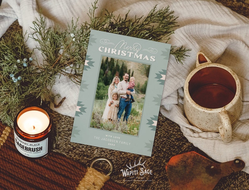 May include: A teal blue Christmas card with a geometric pattern border. The card features a photo of a family of four standing in a field. The text "Merry Christmas" is written in a cursive font at the top of the card. The text "With love, The Jacobsen Family 2022" is written at the bottom of the card.