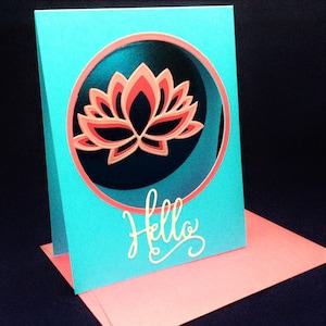 May include: A turquoise card with a pink and white lotus flower in a circle. The card has the word "Hello" written in white cursive.