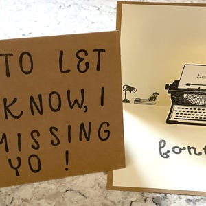 Puede incluir: Una tarjeta de felicitaci&oacute;n hecha a mano con un dise&ntilde;o de m&aacute;quina de escribir emergente. La tarjeta est&aacute; abierta, revelando una ilustraci&oacute;n de m&aacute;quina de escribir vintage con la palabra "hello" en el papel. La tarjeta dice "fontly" en la parte inferior. La tarjeta adjunta dice "J ST TO L& YO KNOW, I AM MISSING YO!"
