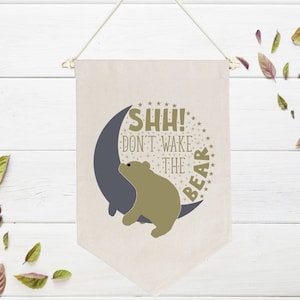 May include: A beige canvas banner with a crescent moon and a brown bear. The banner reads "Shh! Don't wake the bear".