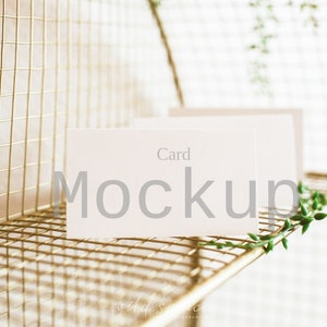 May include: A white card mockup with the text "Card Mockup" on a gold wire rack with green foliage.