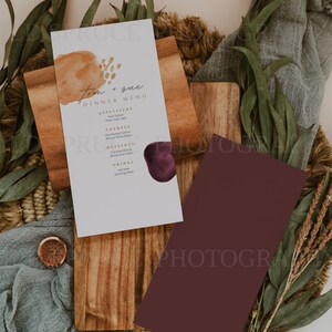 K&ouml;nnte beinhalten: Eine wei&szlig;e Karte mit einem Abendessen-Men&uuml; f&uuml;r Tom und Sue. Das Men&uuml; bietet Vorspeisen, Hauptgerichte, Desserts und Getr&auml;nke. Die Karte hat einen Aquarell-Hintergrund mit einem braunen und violetten abstrakten Design.