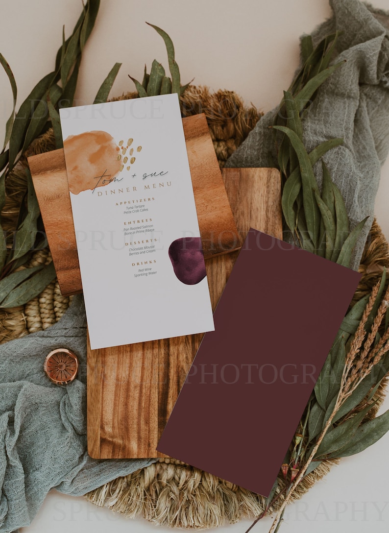 K&ouml;nnte beinhalten: Eine wei&szlig;e Karte mit einem Abendessen-Men&uuml; f&uuml;r Tom und Sue. Das Men&uuml; bietet Vorspeisen, Hauptgerichte, Desserts und Getr&auml;nke. Die Karte hat einen Aquarell-Hintergrund mit einem braunen und violetten abstrakten Design.