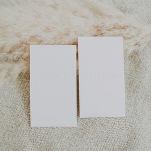 May include: Two blank white cards on a beige textured surface with a dried pampas grass plume.