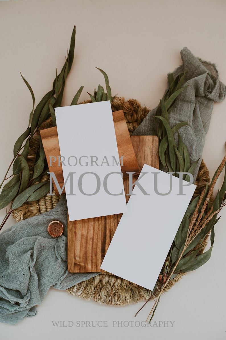 K&ouml;nnte beinhalten: Zwei leere wei&szlig;e Karten auf einem Holzbrett mit einer gewebten Basis, umgeben von Gr&uuml;n und einem blauen Stoff. Der Text "PROGRAM MOCKUP" ist auf dem Brett sichtbar.