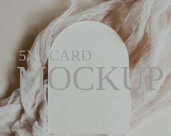 Può includere: Un mockup di una carta bianca con bordi arrotondati, con il testo "5x7 CARD MOCKUP" su uno sfondo beige. La carta è parzialmente coperta da un tessuto leggero di colore marrone chiaro.