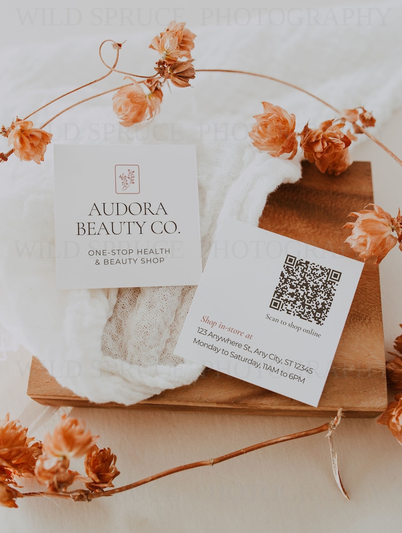Może przedstawiać: Biała wizyt&oacute;wka z tekstem "Audora Beauty Co." i "One-Stop Health & Beauty Shop". Wizyt&oacute;wka zawiera r&oacute;wnież kod QR z tekstem "Scan to shop online" i adresem "123 Anywhere St, Any City, ST 12345". Wizyt&oacute;wka leży na drewnianej powierzchni z suszonymi kwiatami.