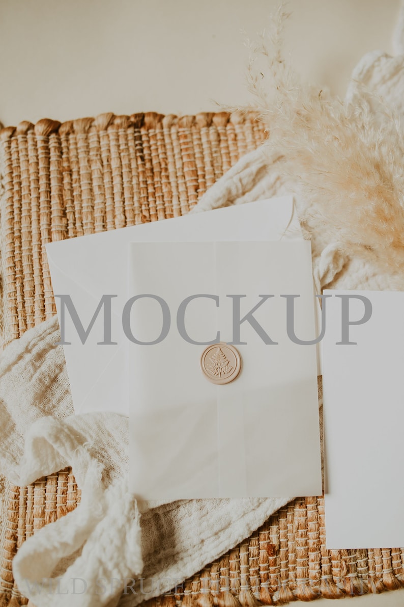 May include: A white envelope with a wax seal on a woven mat with a piece of white fabric and a dried grass plume. The envelope has the word "MOCKUP" printed on it.