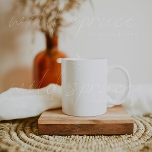 May include: A white ceramic mug sits on a wooden coaster atop a woven round placemat. The mug is blank and ready for personalization.