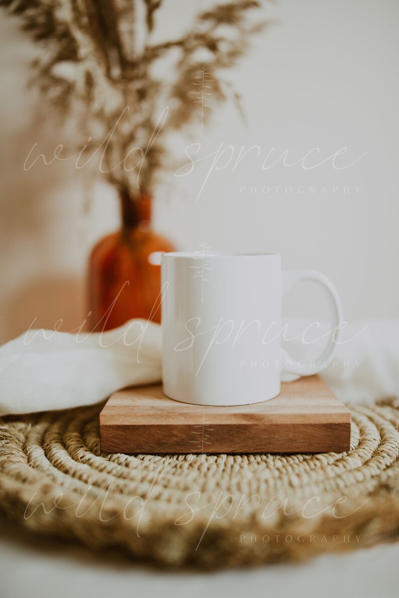 May include: A white ceramic mug sits on a wooden coaster atop a woven round placemat. The mug is blank and ready for personalization.